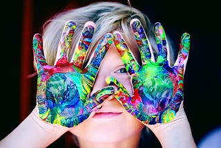 Child with multicolored paint on hands.