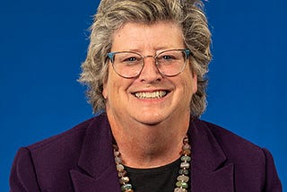 A white woman in glasses smiles in her headshot