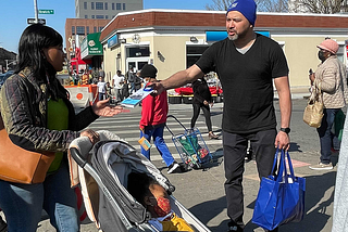 NYC DCWP street team member distributes an NYC Free Tax Prep flyer about claiming tax credits to a parent pushing a stroller in Brooklyn during the 2022 tax filing season.