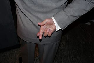 Photograph of the back of a white man who is crossing his fingers (behind his back)