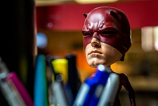 A photo of a Daredevil bobble head on a desk, blurry pens in the foreground