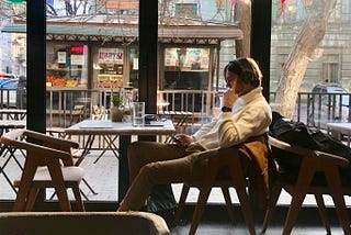 A person in a chair in front a window on a phone, looking at another phone. What are you doing and why are you doing it?