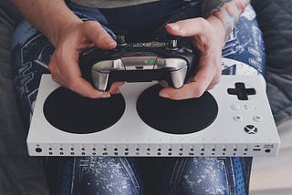 the xbox adaptive controller in my lap, with my hands resting on it holding an xbox elite controller over top