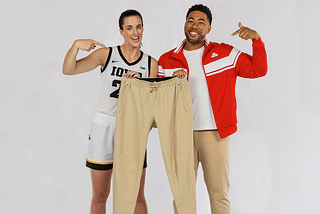 Picture of Caitlin Clark and Jake from State Farm smiling together and holding up a pair of sweat-pants.