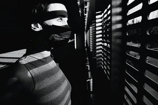 Someone scared and looking through blinds out of a window.