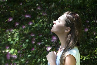 A woman breathing consciously in front of a flowering bush