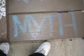 “Myth” written on the ground in blue color with white colored shoes besides it.