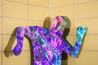 Photograph of the author in front of a khaki-colored tile wall wearing a iridescent mylar suit.