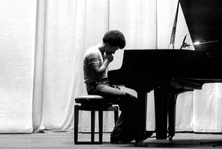 Keith Jarret sitting at a piano, staring at the keys