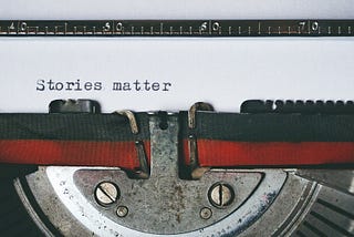 Top of a typewriter showing ribbon and paper. “Stories Matter” is typed onto paper
