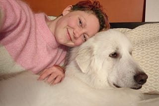 The author laying in bed and slightly on her big white fluffy Great Pyrenees dog