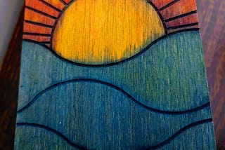 The lid of a handmade wooden box painted with a bright sunrise.