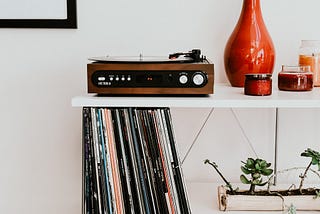 Record player playing a vinyl on top of a shelf containing records