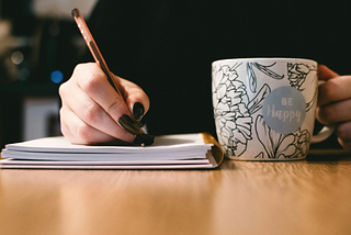 Hand With Pencil On A Book With Cup Beside