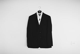 A suit, hung up against an unadorned white wall.