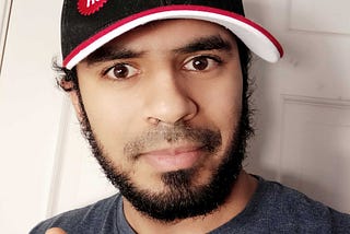 A handsome man with a great beard is seen wearing a General Assembly hat and giving a thumbs up.