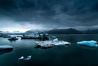 Small icebergs floating in the ocean under dark, cloudy skies.