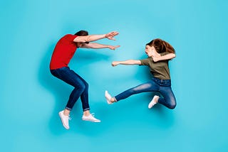 A crazy young couple in casual clothes fight physically in front of a blue background.