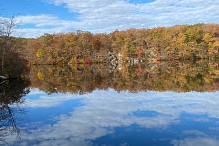 The changing colors of leaves are reflected in a lake. Photo by author.