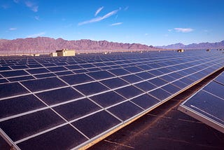 A long row of solar panels in the foreground and a mountain range in the background.