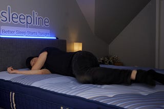 A person is lying on a bed. He appears to be doing a trial of a mattress or brand of bed since the brand is shown on a lighted sign above the bed.