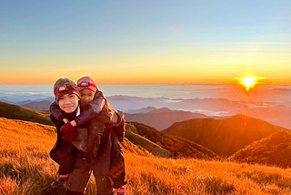 Teenage boy carrying a little girl against the backdrop of an orange sunrise, mountains and a sea of clouds