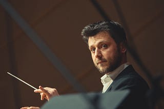 A conductor holding a baton and looking at the camera