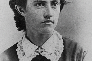 Portrait of woman in late 1800s with cropped dark hair, brown eyes, wearing a lace color and dark clothes.