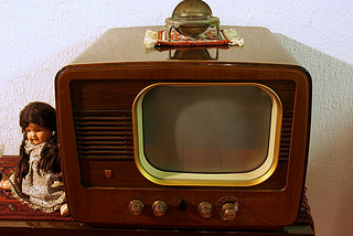 An old Phillips black and white television set next to a doll