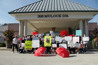 A large crowd of people outside Newmarket Municipal Offices with signs demanding the discriminatory bylaw ends (e.g. Rights Not Rescue). Some of them have red umbrellas.