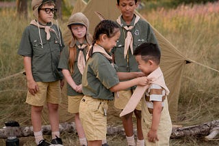 Children dressed in scout uniforms. A girl is helping a little boy tie his neckerchief.