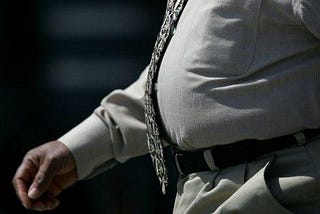 Cropped image of overweight man walking. Wearing a brown tie and kaki shirt and trousers.