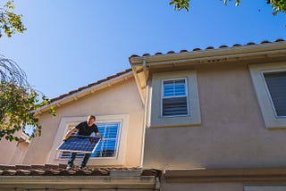 A man holding a solar panel on the roof of a house.