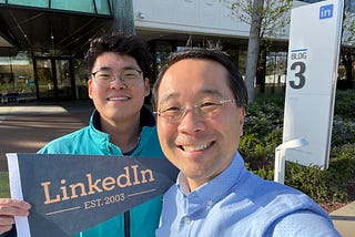 Two men in front of LinkedIn office building holding a sign that says “LinkedIn est. 2023"