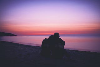 woman and man sitting and watching the sunset on the water