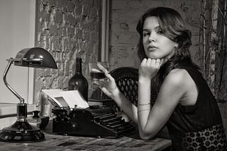 Elegant woman in black with an old typewriter and a drink