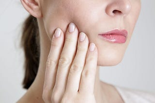 Image of a woman pushing in on the outside of her cheek, as if she has a toothache.