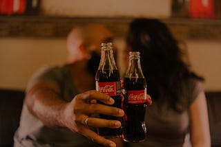 Two people hold up Coca-Cola bottles.