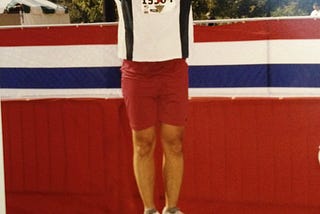 Kevin standing on a short award platform shortly after the marathon wearing his participation medal and raising his arms in the air in a sign of victory