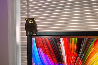 A brown foam bear figure perched on the corner of a computer monitor