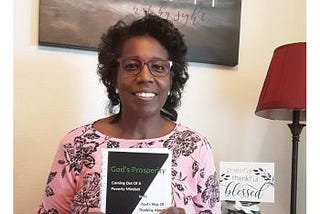Nek’ka Migel, author holding the book God’s Prosperity, a Christian book about faith and money.