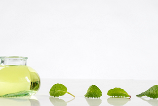 Container of peppermint oil with peppermint leaves trailing behind it.