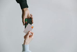 A person holding a credit card over to tap a card reader and pay for a purchase