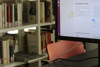 A computer where you can see a research on energy poverty. The computer is on a desk, in a library full of books