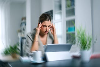 Young woman working from home, holding head in pain with room spinning