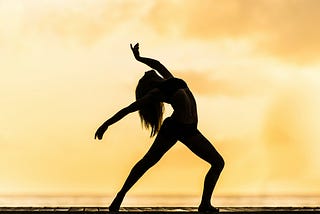 Silhouette of a woman doing yoga against  a yellow background.