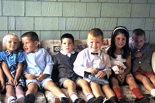 Seven smiling 5 and 6-year-old boys and girls, dressed for a party, squeezed side-by-side on a couch
