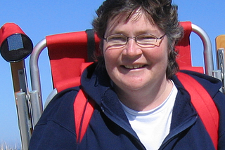 Denise Kendig smiling at camera with red beach chair backpack and blue skies