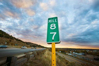 Mile marker on a road side with a bright blue sky above it.