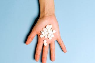 Hand lying palm-side up with several white pills in the centre of the palm.